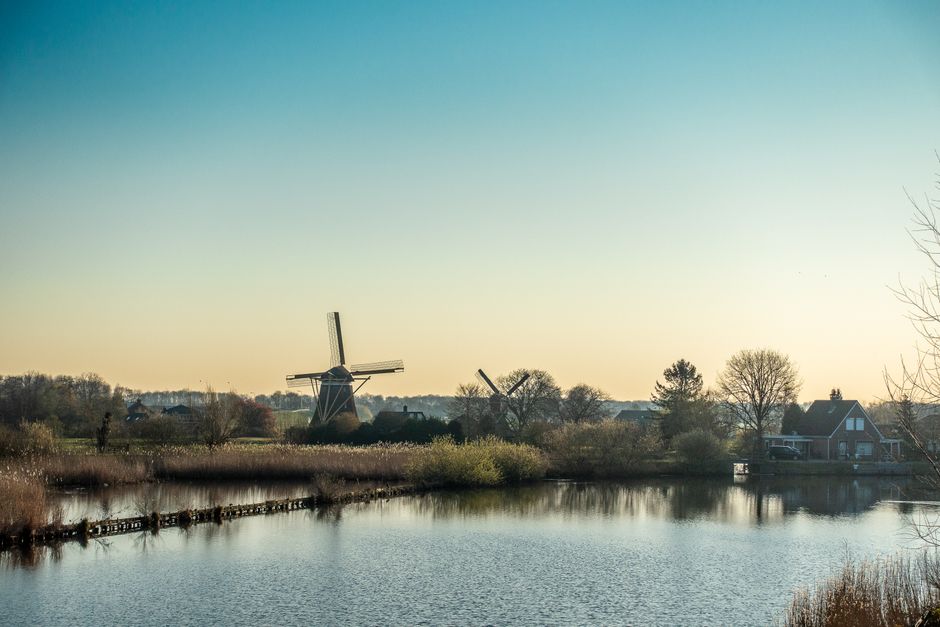 Picturesque landscape featuring classic windmills by a tranquil river under a clear sky.