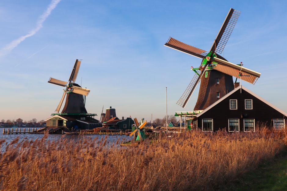 Scenic view of iconic Dutch windmills near water at Zaanse Schans, Netherlands, during sunset.